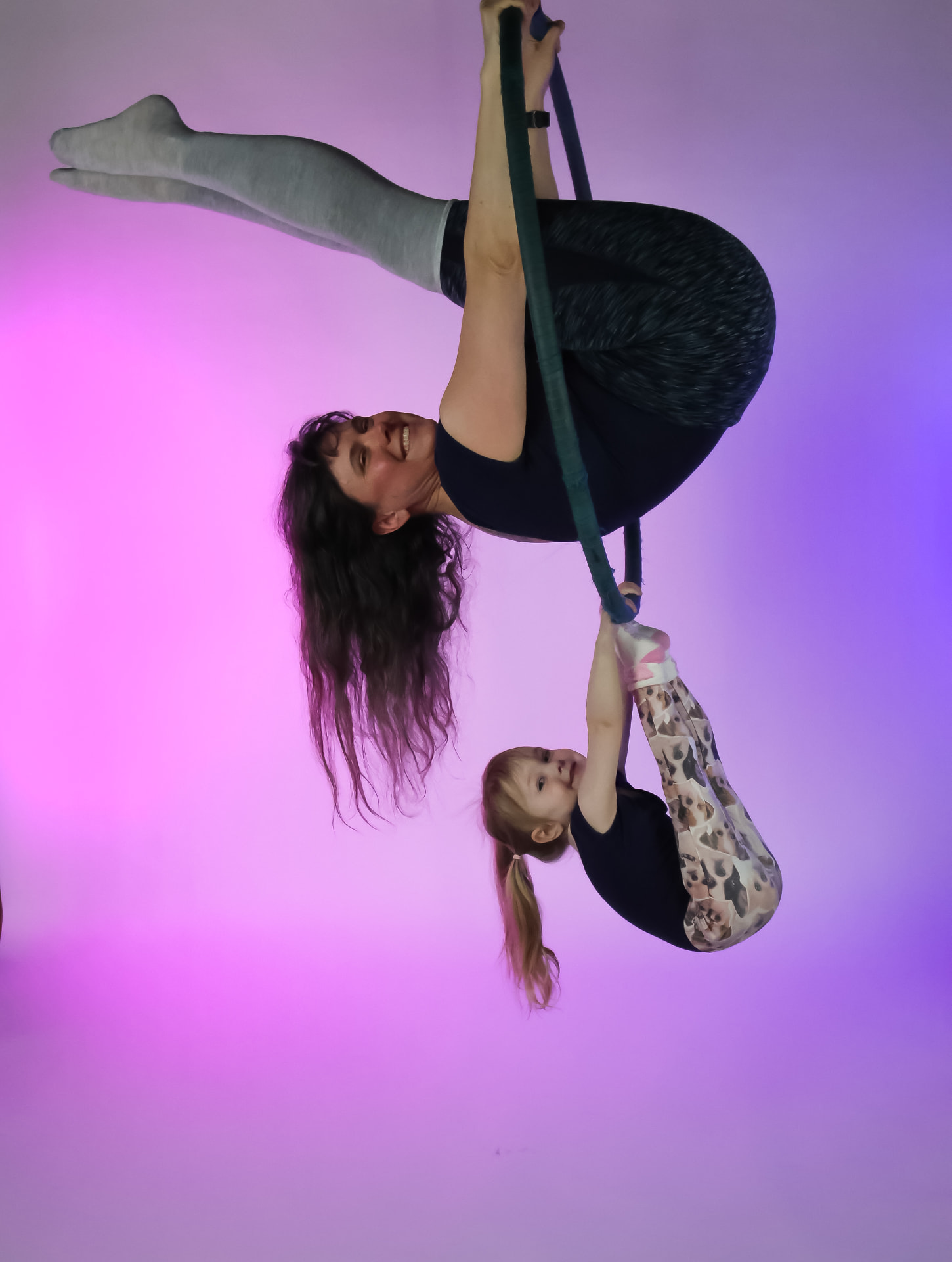 A mom and daughter hanging upside down together from an aerial hoop