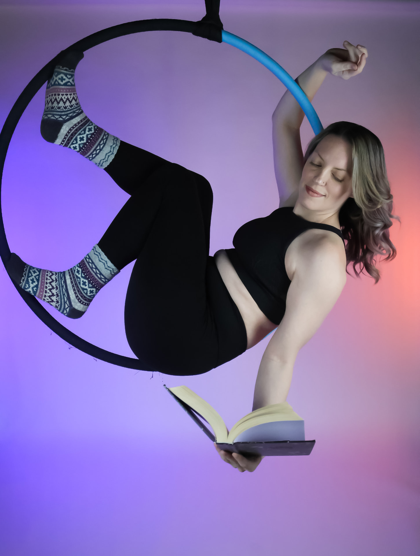 Aerialist reading a book while reclining in a lyra hoop at Flexibility in Flight
