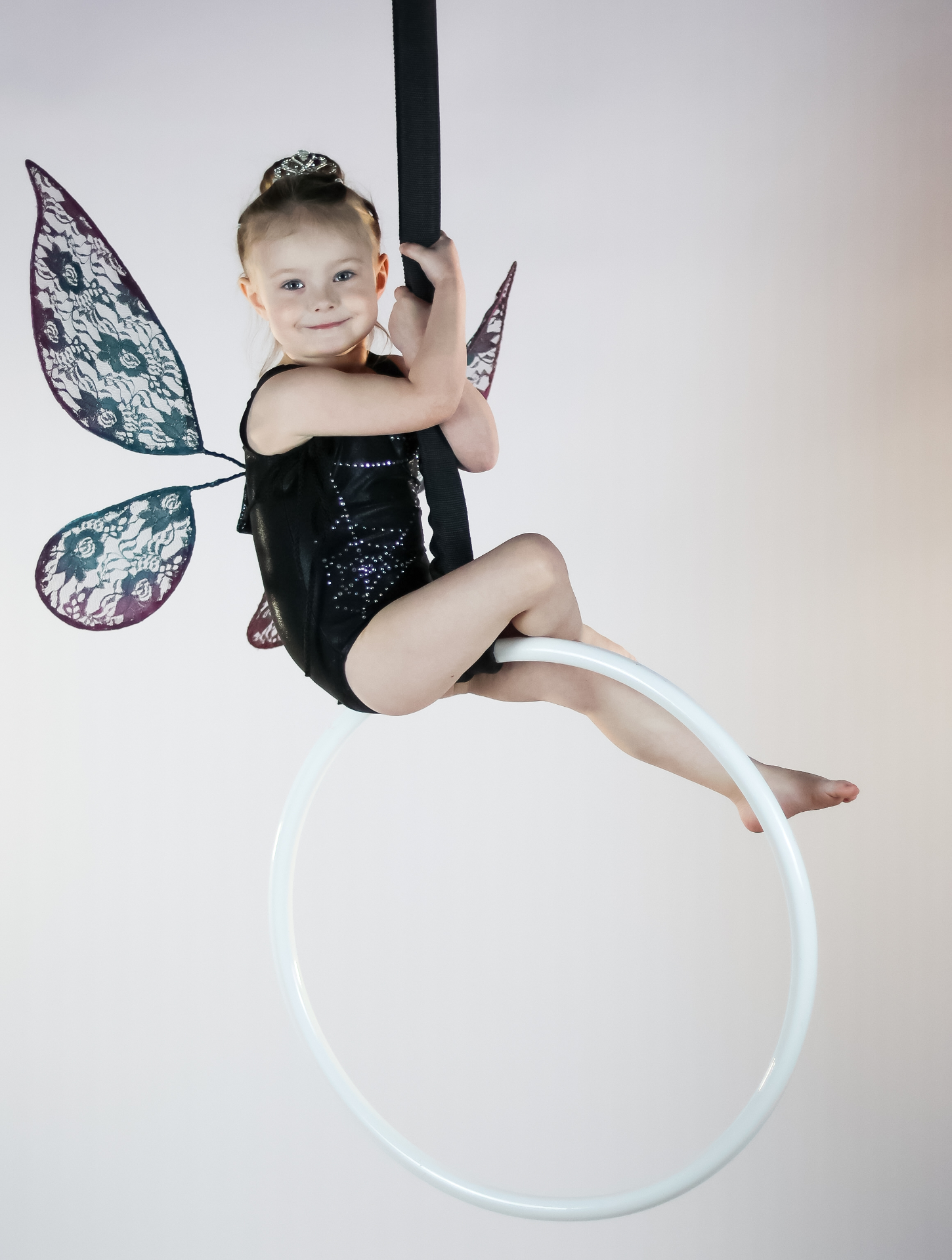 Young aerialist with fairy wings sitting on a lyra hoop