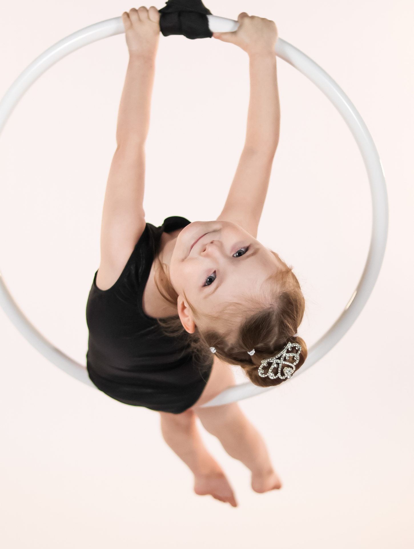 Smiling child hanging upside down inside an aerial lyra hoop
